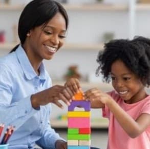 Une tutrice construit une tour de cubes avec une petite fille